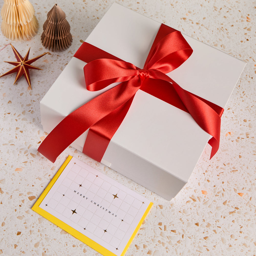 White gift box wrapped in red satin ribbon with a personalised Merry Christmas notecard