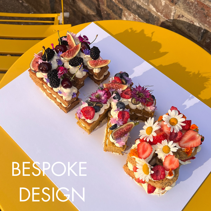 Letter Cake spelling E K B, decorated with fruits and edible flowers. London. 