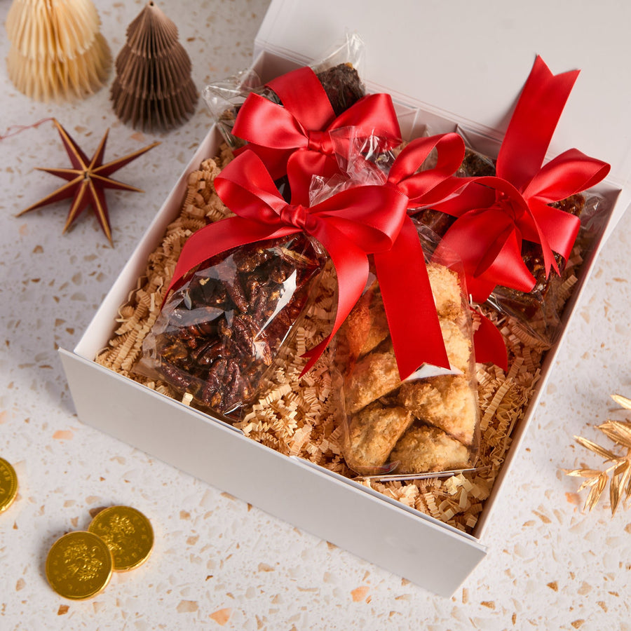 Open gift hamper with pecan florentines and caramelised pecans, coconut macaroons, malted tiffin, tied with red satin ribbons